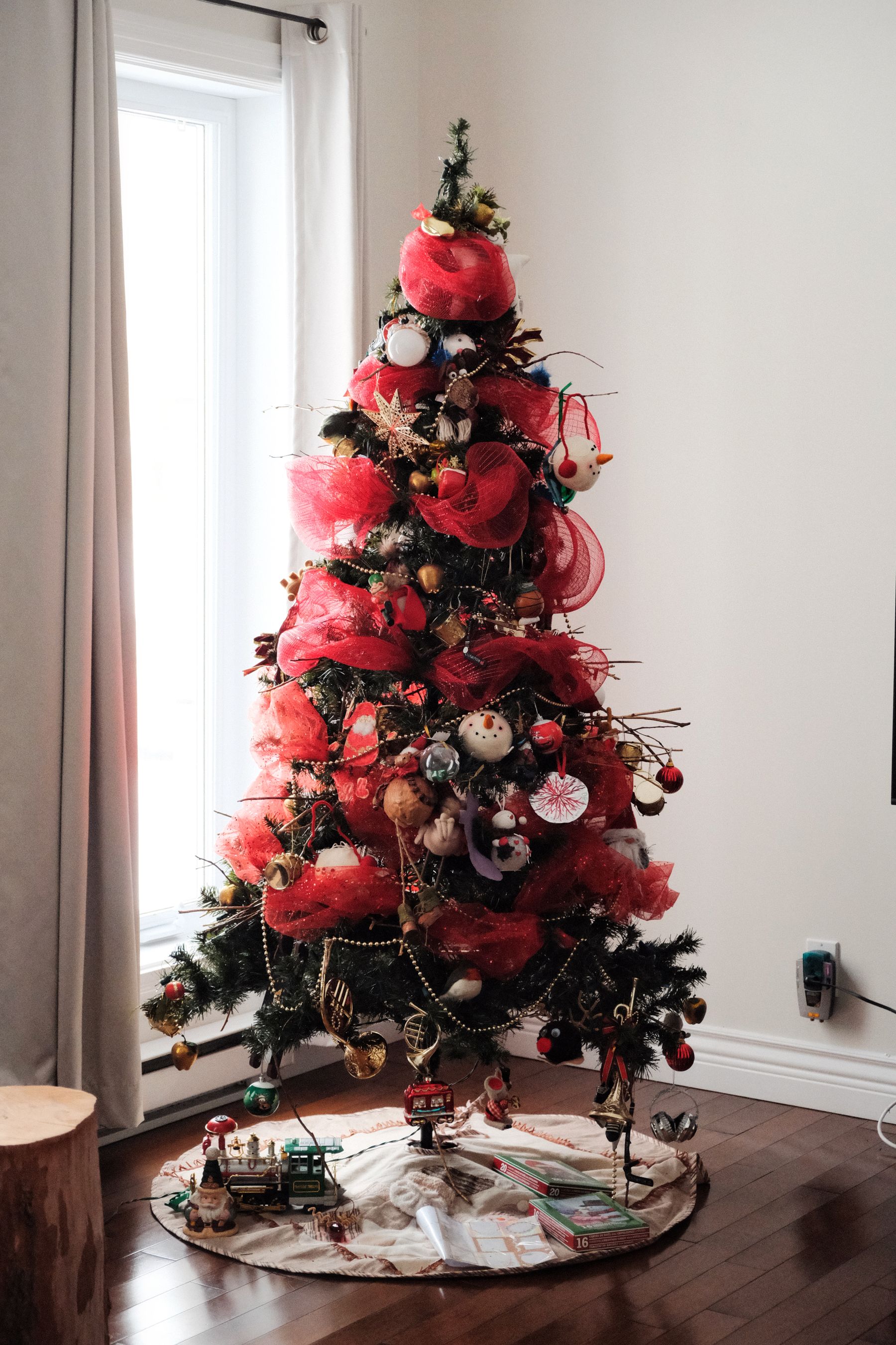 Decorated Christmas tree with layered red and gold ornaments in a warm living room