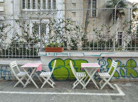 Outdoor café scene with white tables and chairs, urban graffiti art.