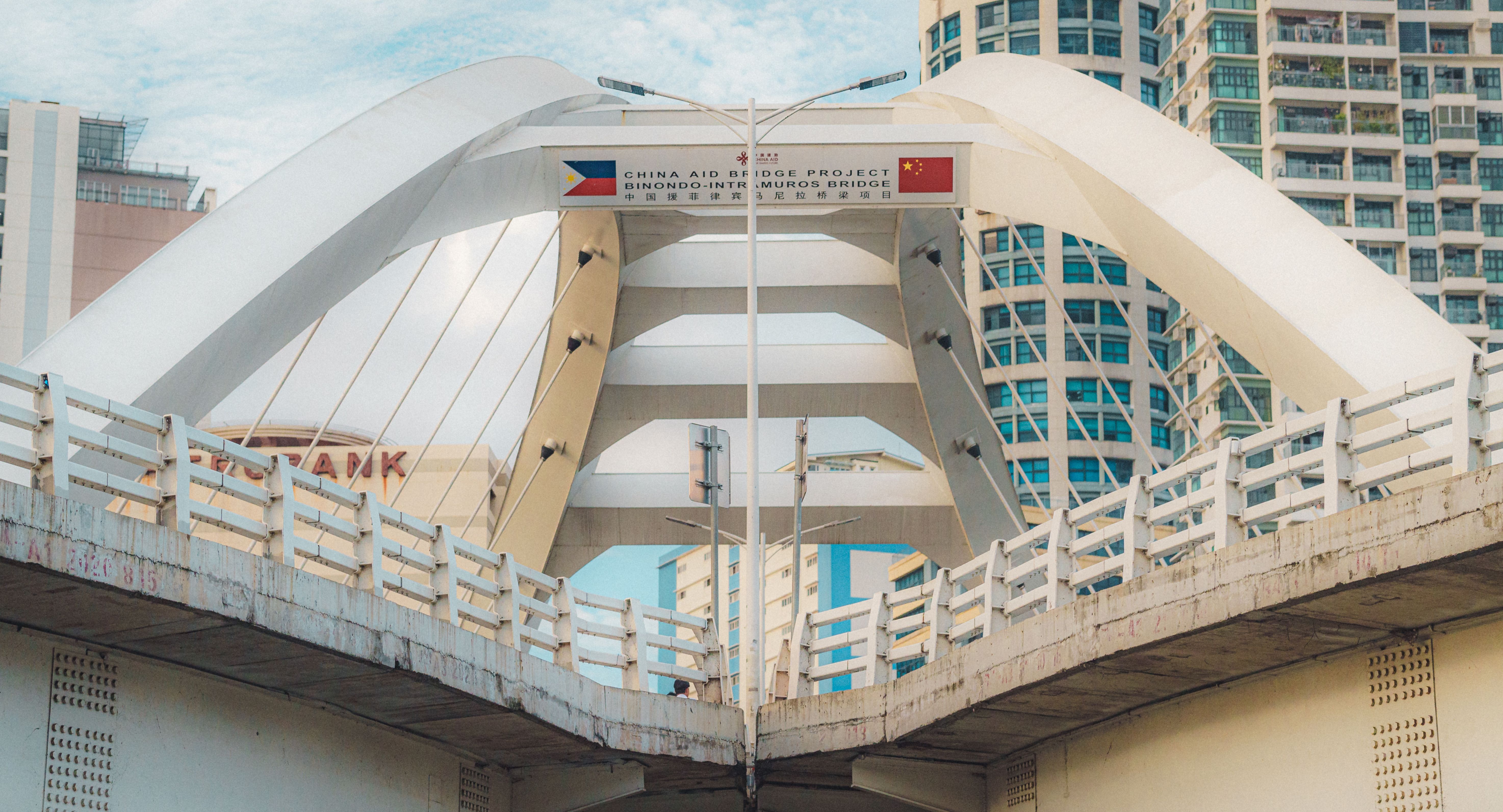 Modern bridge with arched design spanning a river, with city buildings in the background.