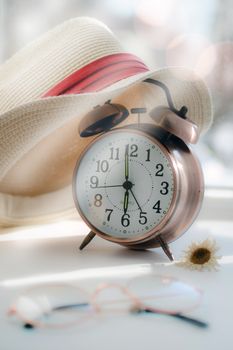 Charming scene with a vintage alarm clock, straw hat, glasses, and a small flower.