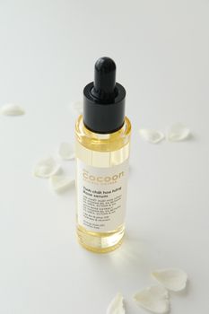 Cocoon rose serum bottle with petal accents on white surface, minimal style.