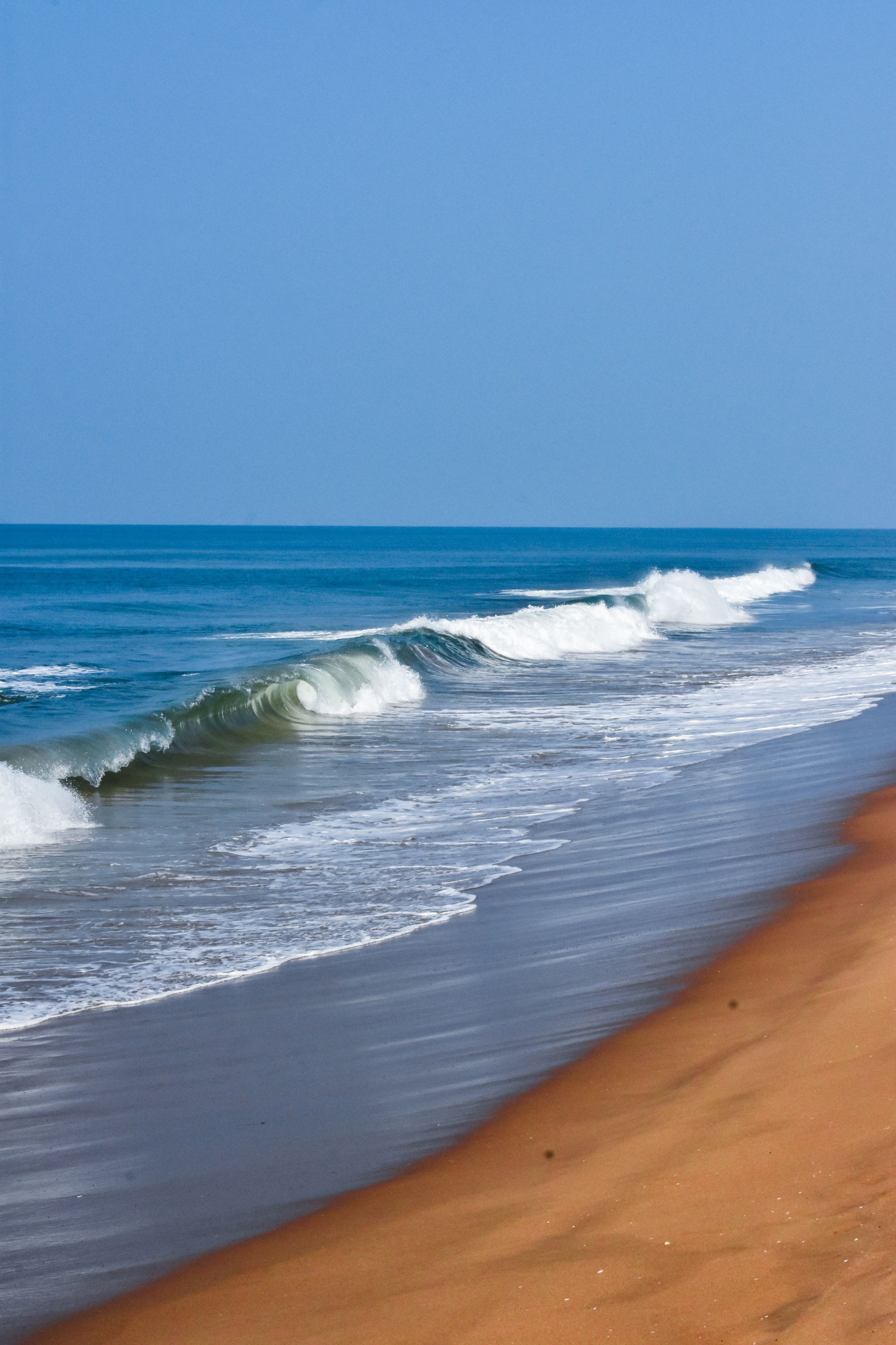 Serene seascape showcasing gentle waves lapping the sandy shore under a clear blue sky.