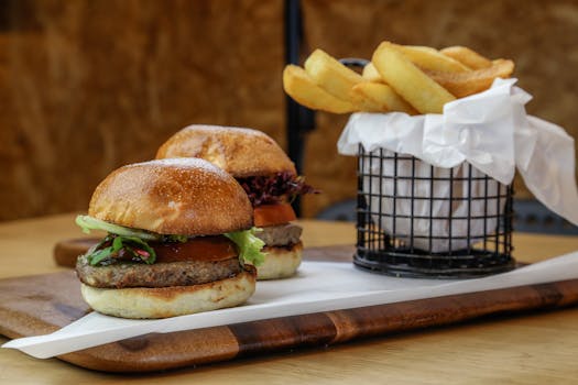 Close-up of appetizing burgers with fries served on a wooden board.