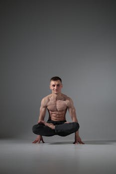 Muscular man performing a yoga pose on a studio floor, showcasing strength and balance.