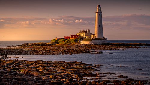 Free Scenic view of a lighthouse by the sea at sunset with golden skies. Stock Photo