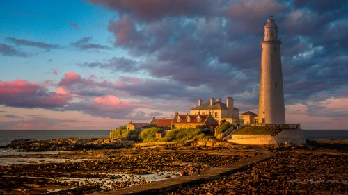 Free Beautiful lighthouse and buildings under dramatic sunset sky on a rugged coastline. Stock Photo