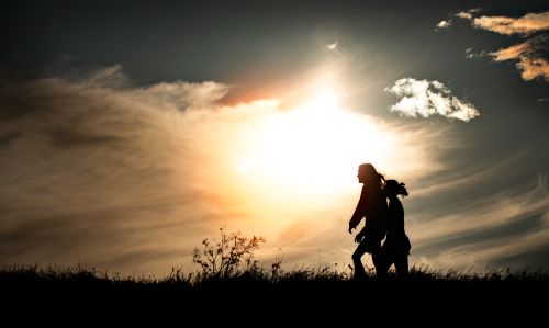 Free Silhouette of two people walking during a vibrant sunset with dramatic clouds. Stock Photo