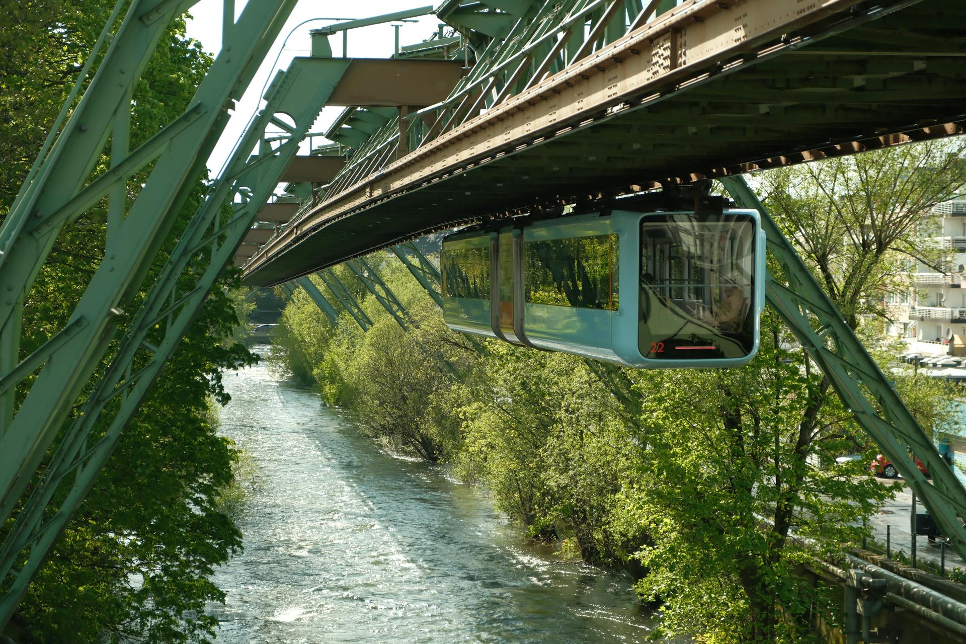 Iconic Wuppertal Schwebebahn suspended train travels over a river. Bright spring day.