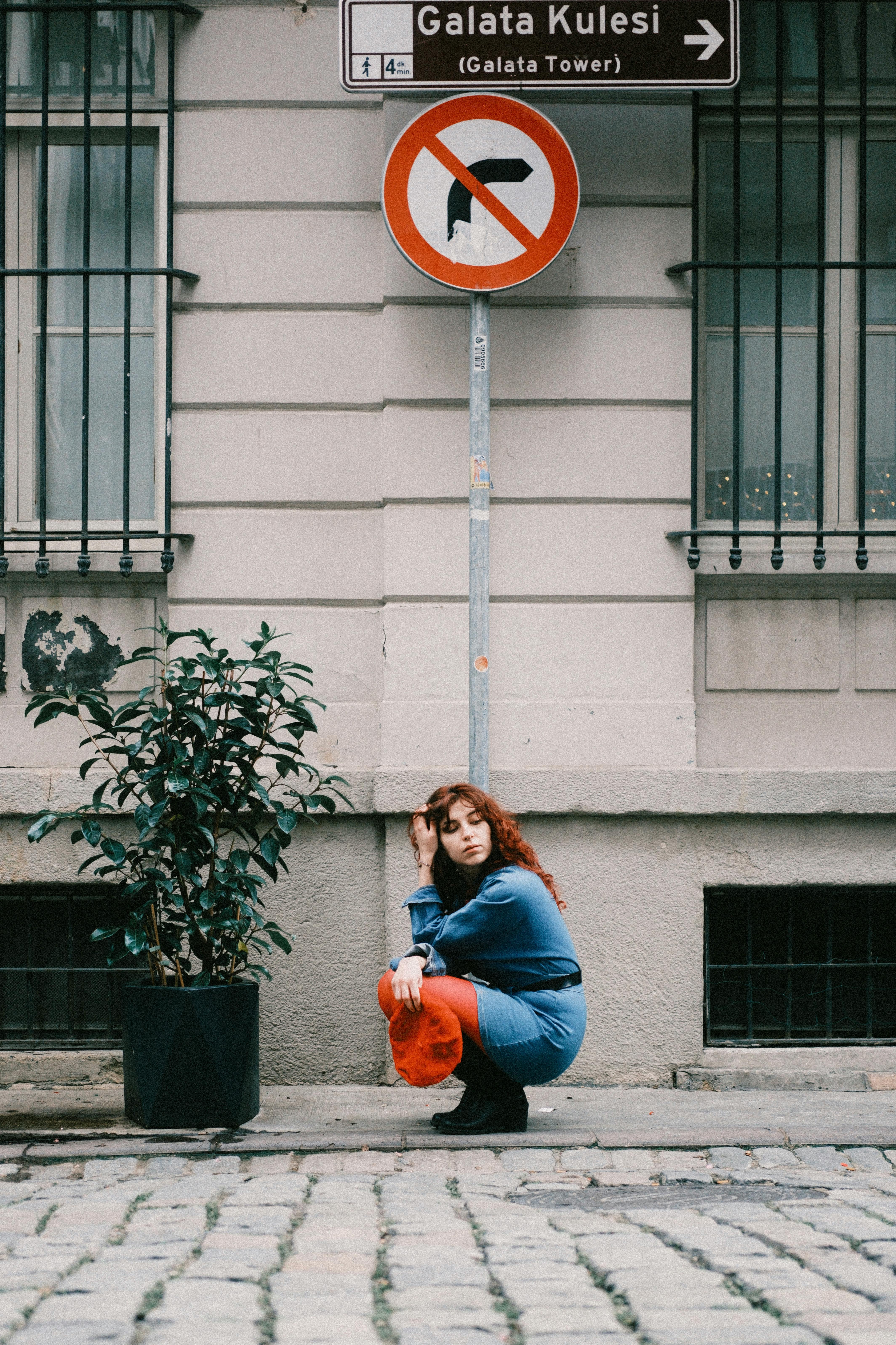 Woman crouching by no entry sign near Galata Tower in an urban setting.