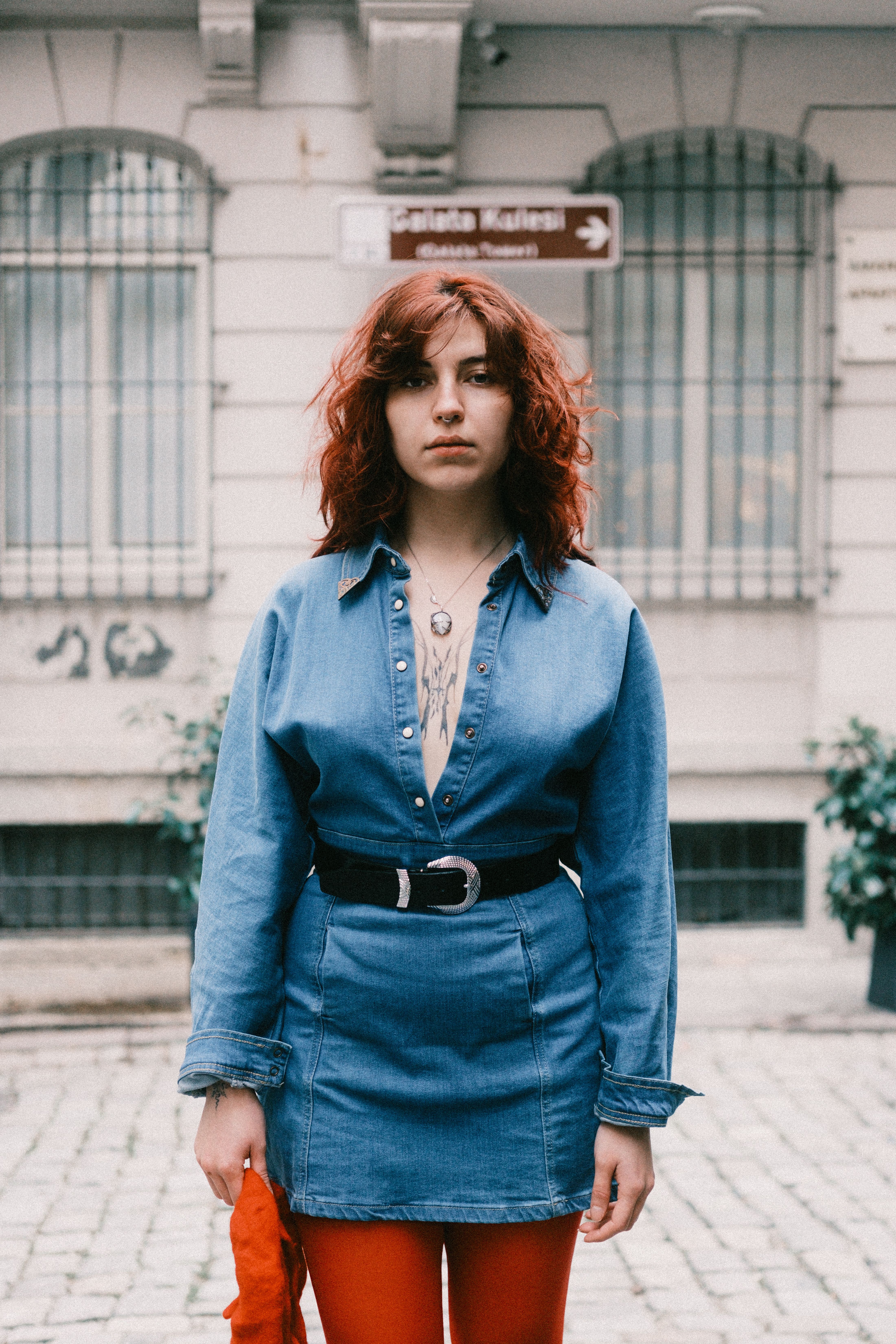 Portrait of a woman in denim dress standing outdoors on a cobblestone street.