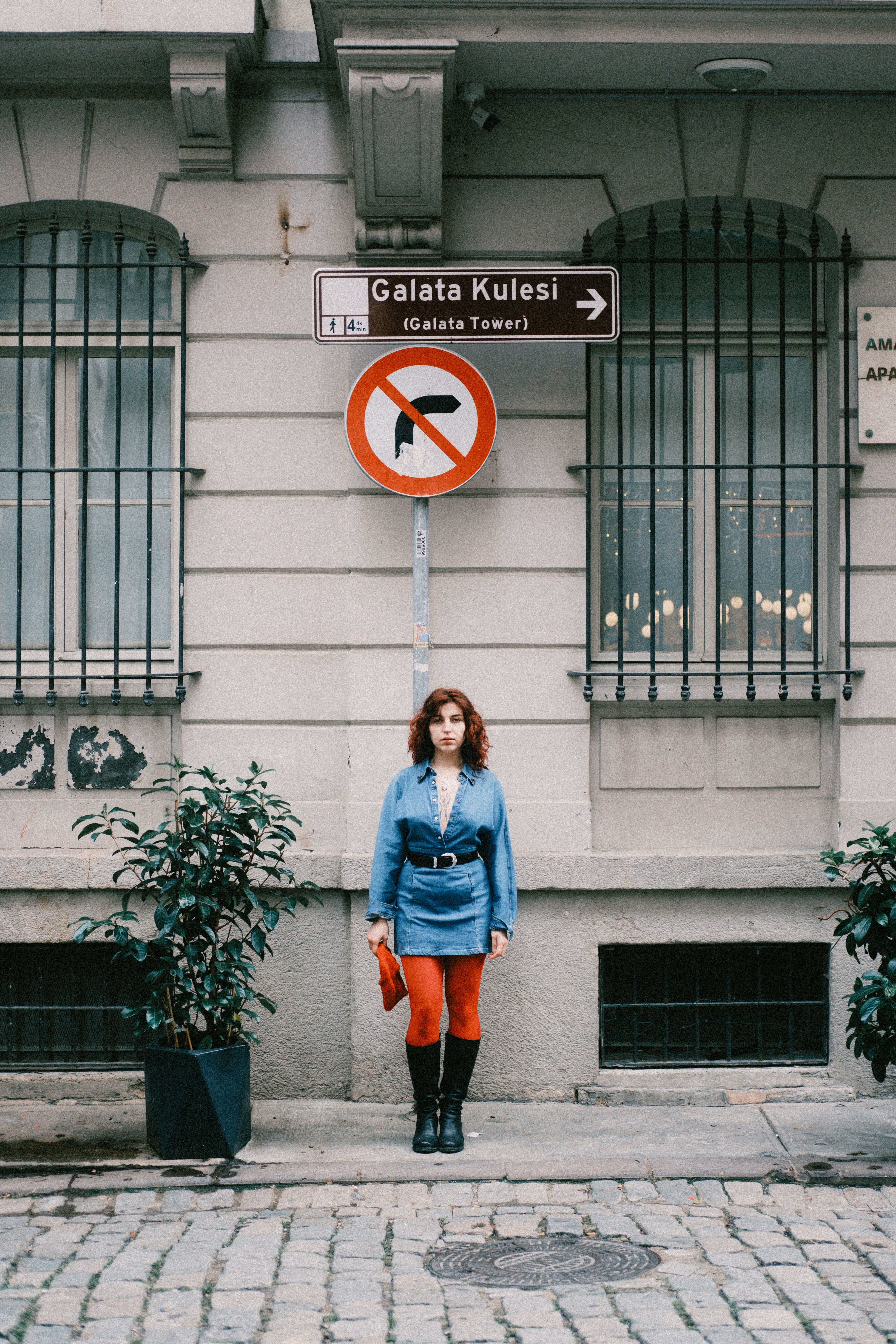 A woman in denim stands by Galata Kulesi sign in Istanbul's street scene.