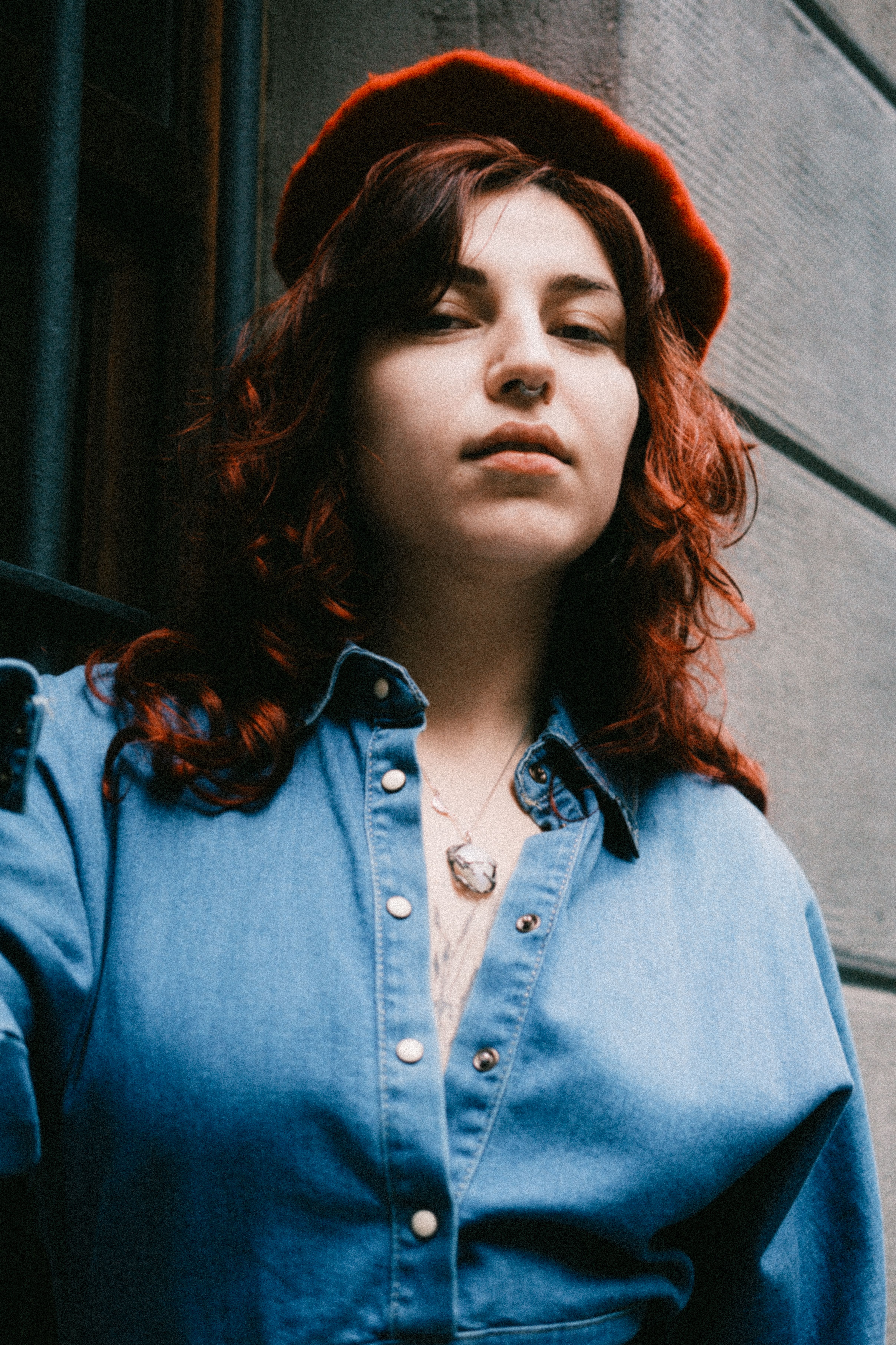 Casual portrait of a woman in a denim shirt and red beret outdoors.