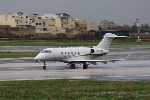 A private jet taxis on a wet runway at an airport with buildings in the background.