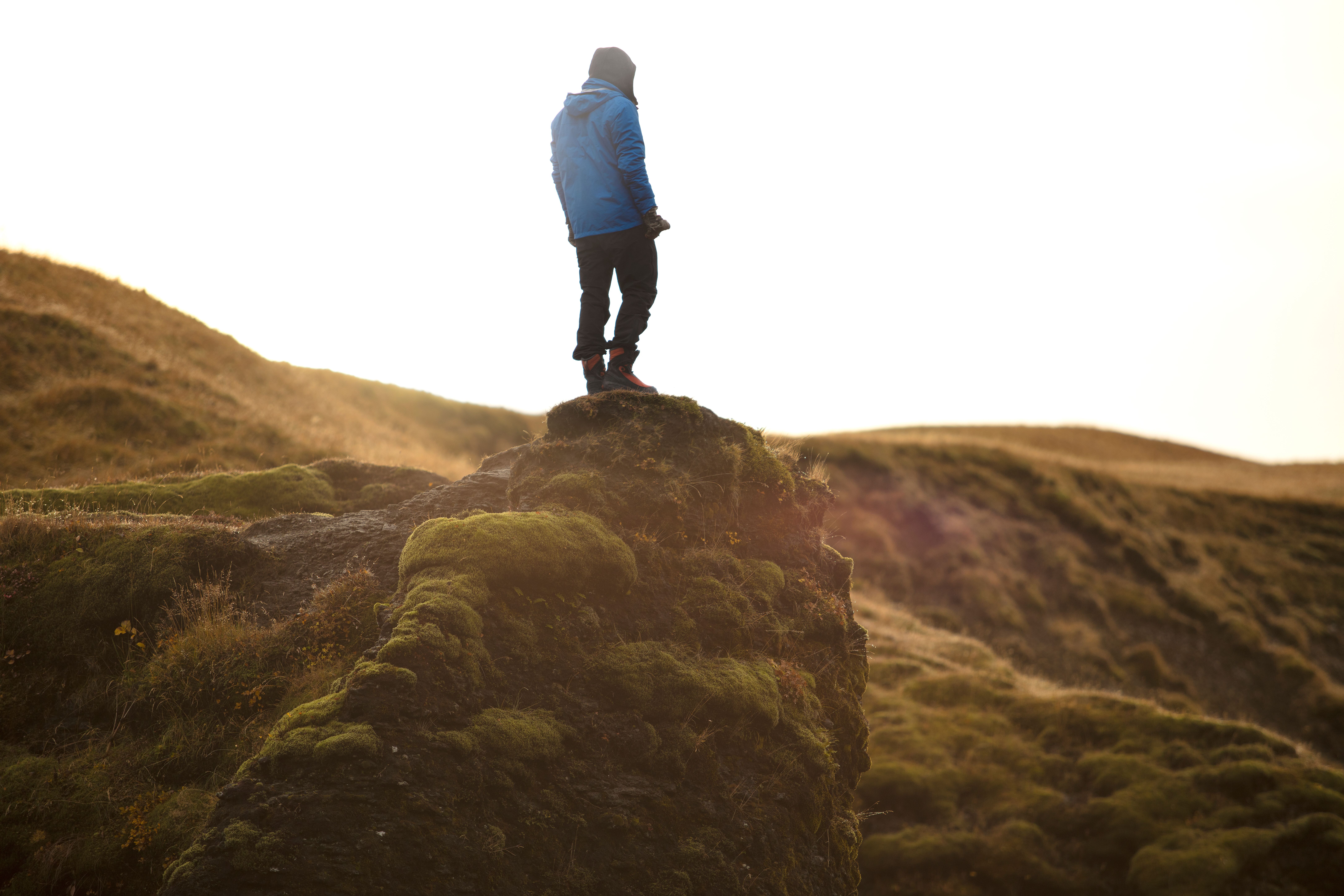 Person standing on moss-covered cliff in the wilderness, enjoying a daytime adventure.