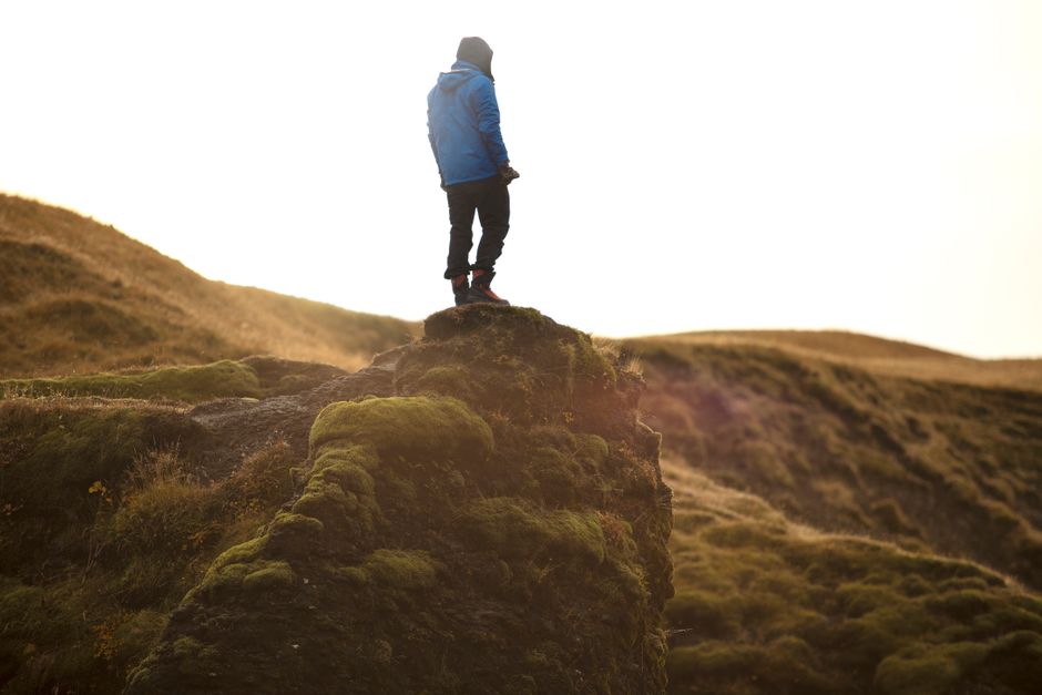 Person standing on moss-covered cliff in the wilderness, enjoying a daytime adventure.