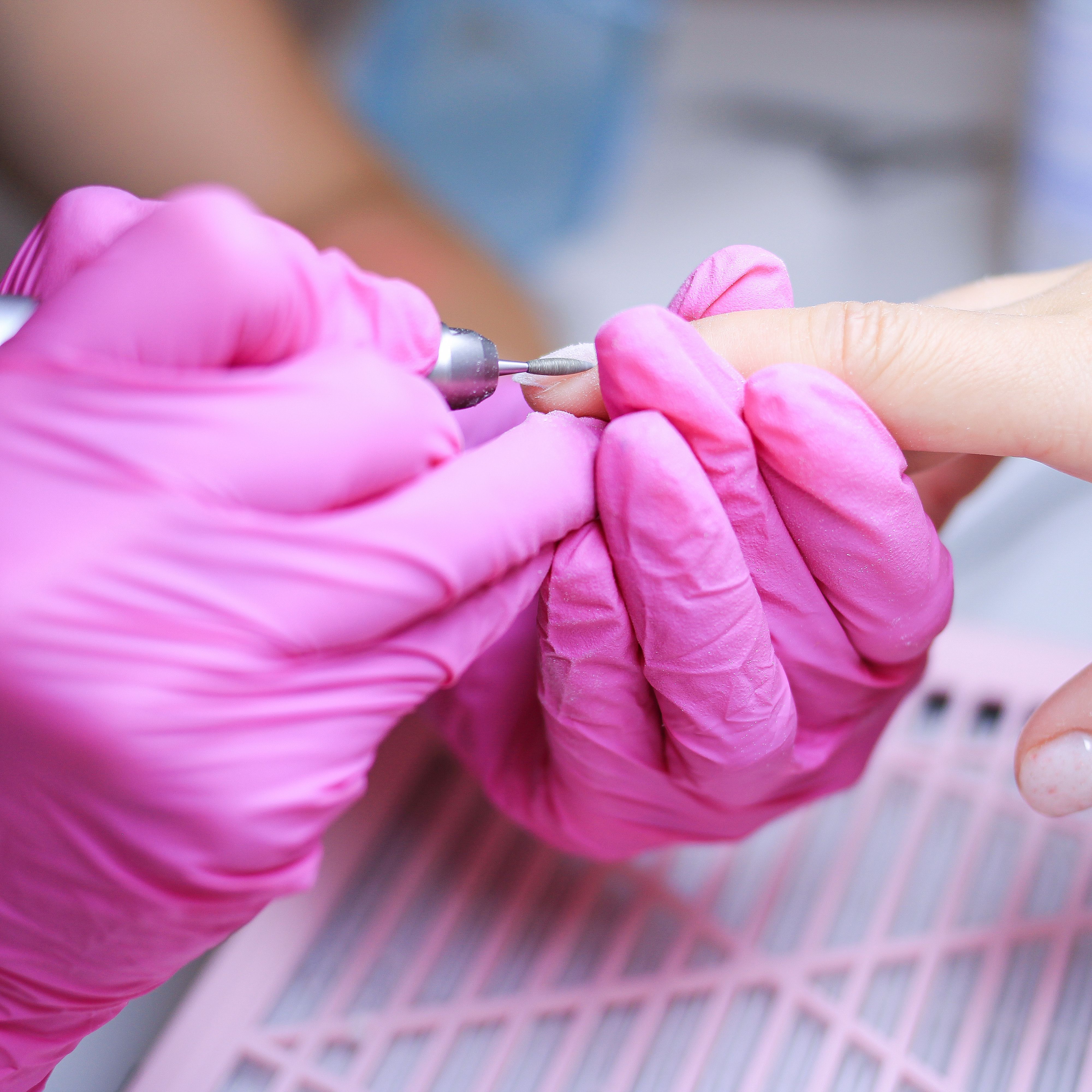 Close-up of a manicure procedure in a Polish salon with technician in pink gloves.