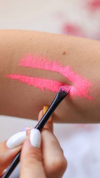 A makeup brush applies vibrant pink lipstick in a creative painting on skin.