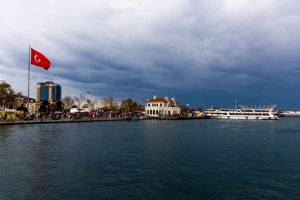Kadıköy waterfront on Istanbul's Asian side, with a Turkish flag and ferries under a stormy sky