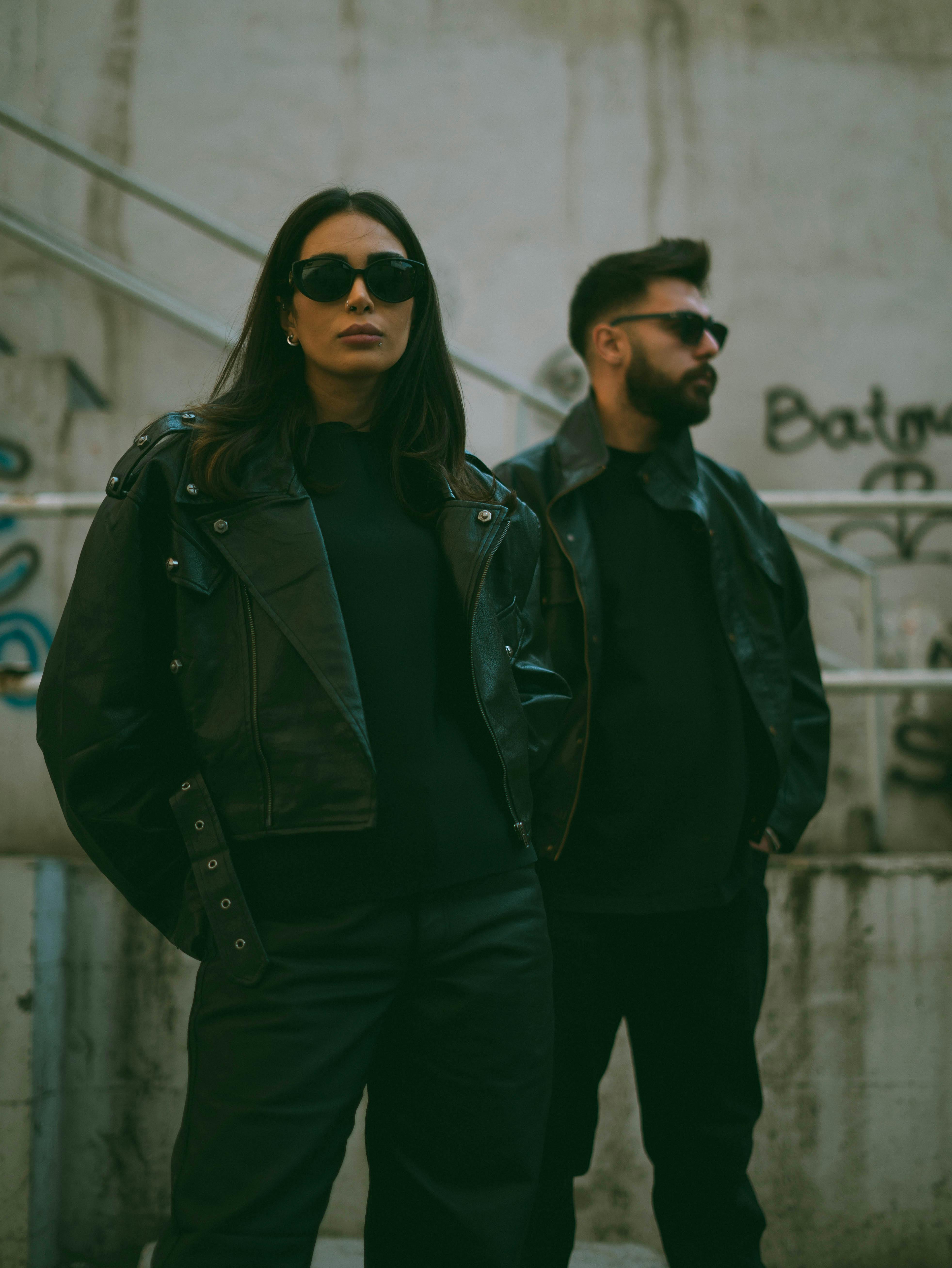Free Fashionable couple in black leather jackets posing in a graffiti-covered urban area. Stock Photo