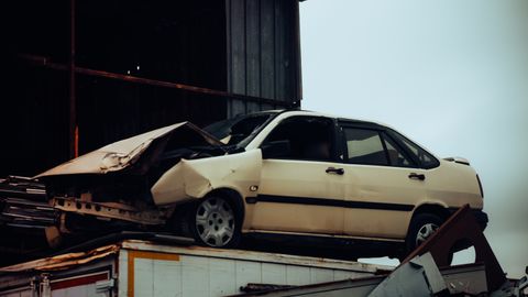 A damaged car sits atop a metal scrap heap, showing a scene of automotive decay.