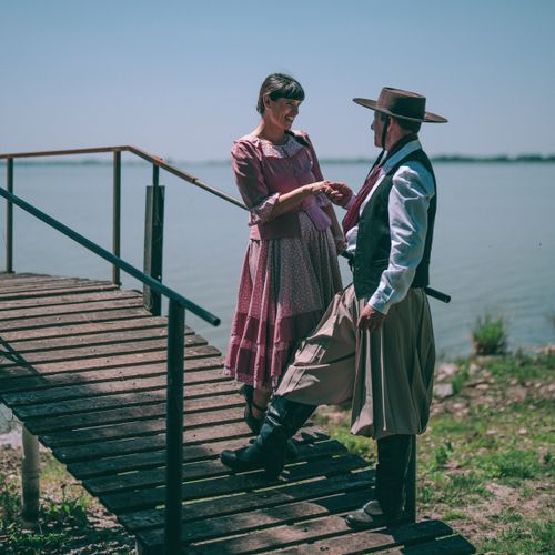 Free A traditional gaucho couple sharing a moment on a wooden walkway by a lake in Chascomús, Argentina. Stock Photo