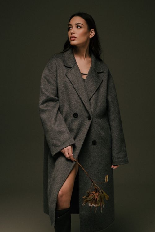 Free Elegant woman in a grey coat holding a flower, captured in a moody studio setting. Stock Photo