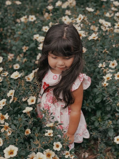 Free A whimsical portrait of a young girl surrounded by vibrant flowers in a serene garden. Stock Photo