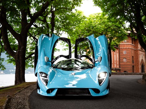 Elegant blue sports car with open scissor doors, parked under lush trees near an ornate building.