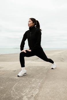 Woman in athletic wear stretching outdoors by a lake in winter.