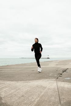 A woman jogs on a concrete pier by the lake against a cloudy sky, capturing a moment of outdoor fitness.
