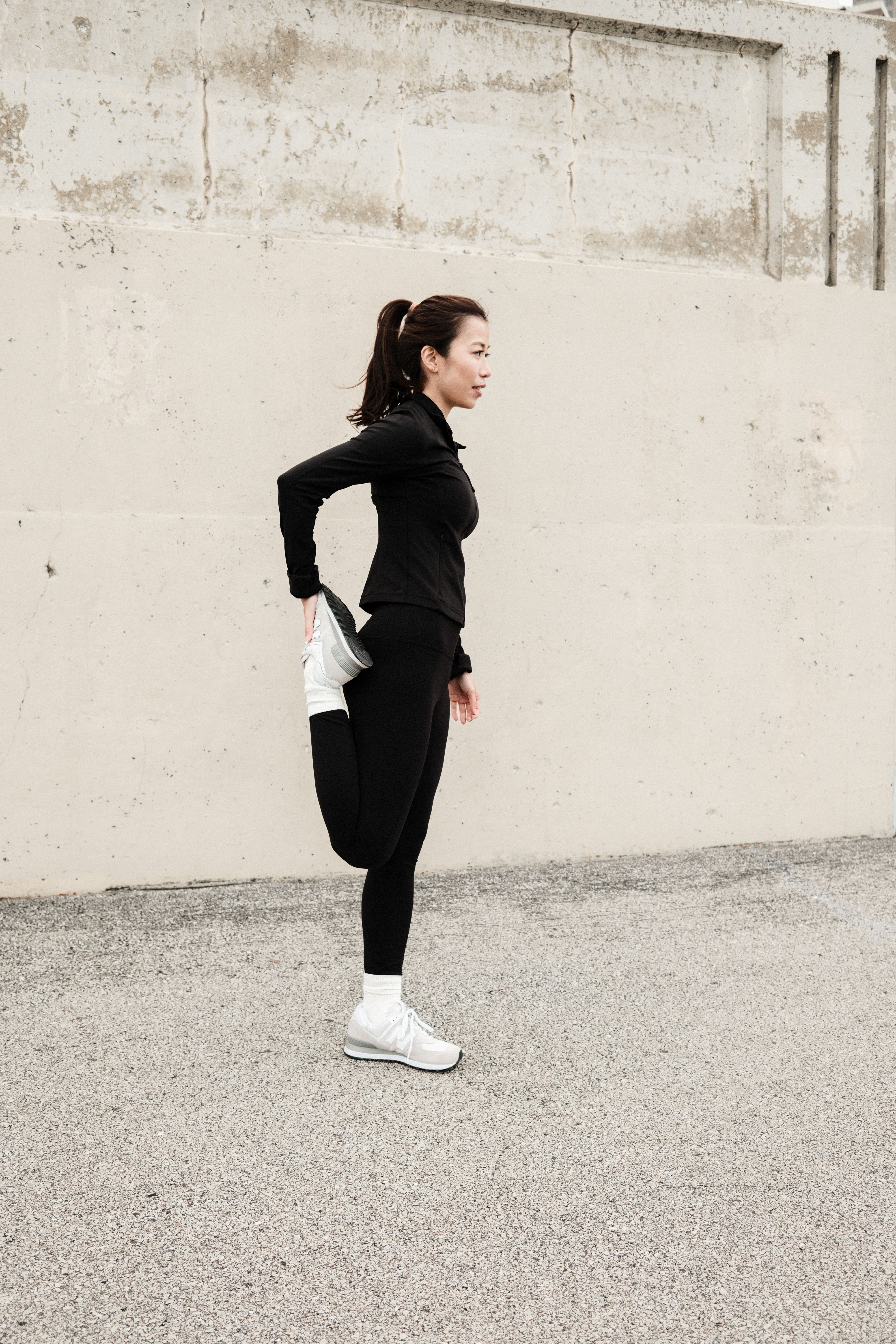 A woman stretches her leg against a concrete wall during a workout, showcasing active lifestyle.