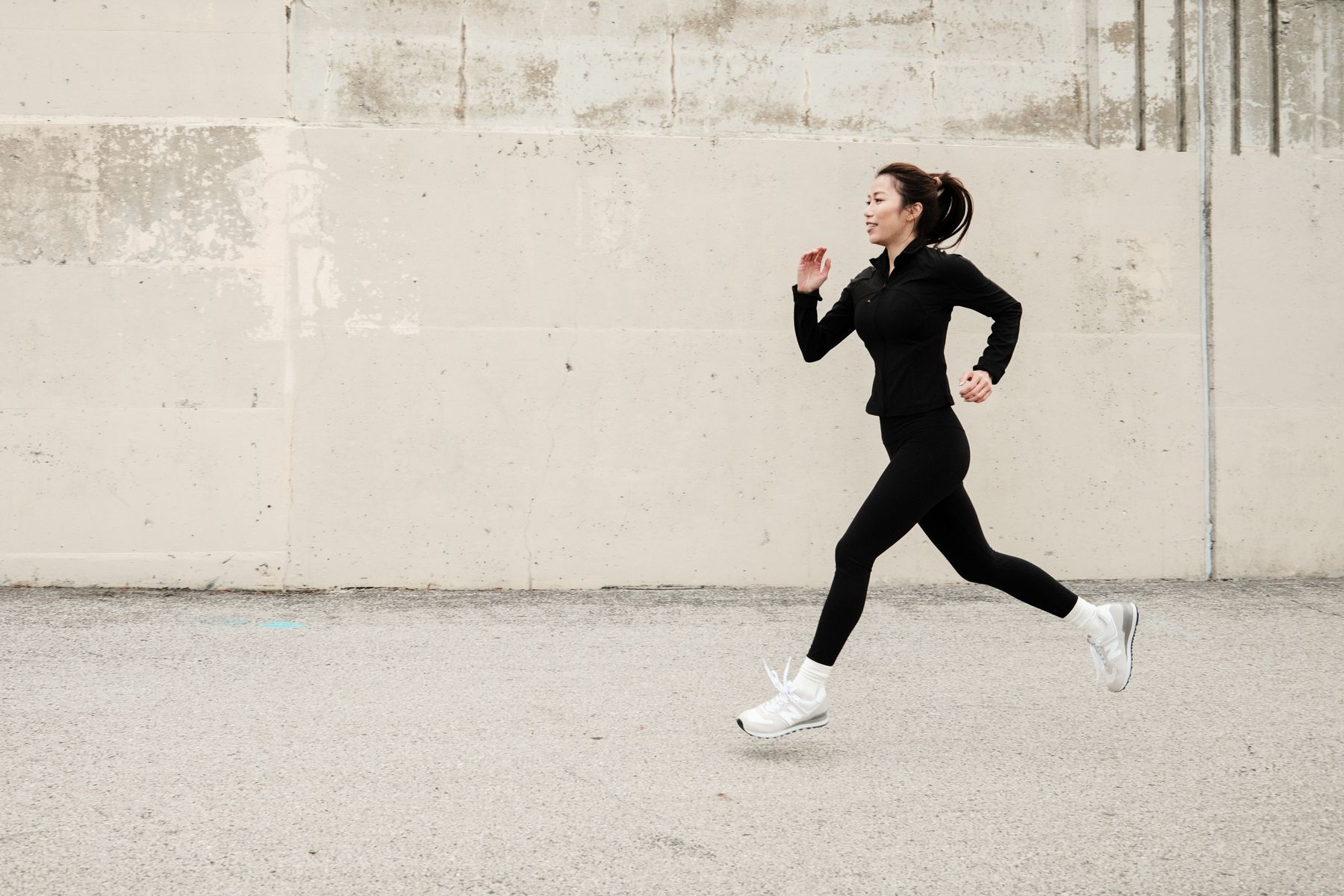 Woman running outdoors in streamlined black activewear and a lightweight training jacket