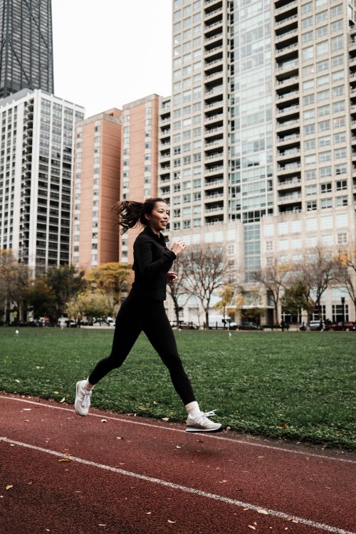 Free A woman in athletic wear jogging on an outdoor track surrounded by city skyscrapers in autumn. Stock Photo