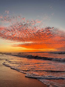 Stunning sunset with vivid orange clouds over a serene beach as waves gently crash.