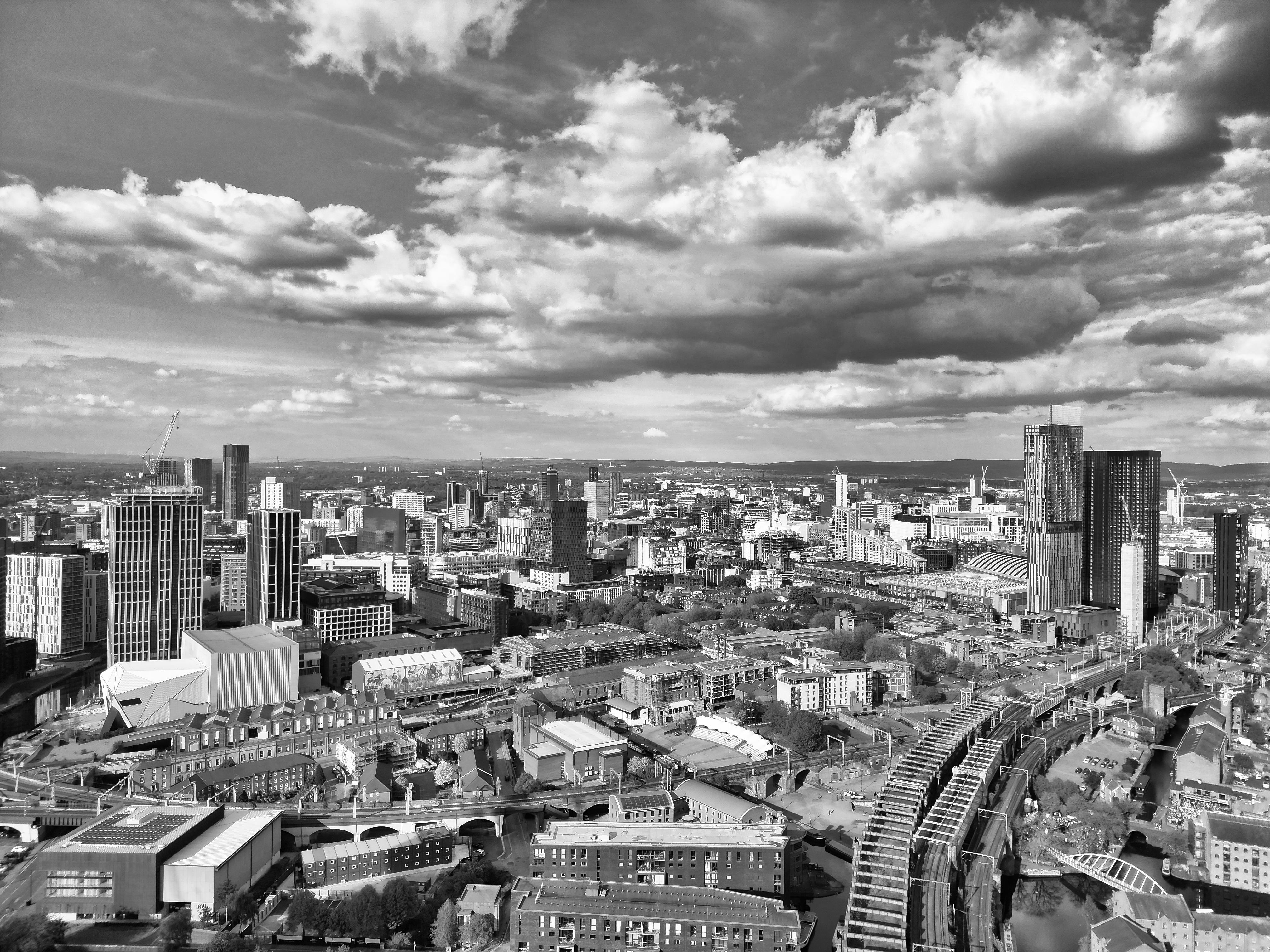 A dramatic black and white aerial view of Manchester's skyline with clouds overhead.