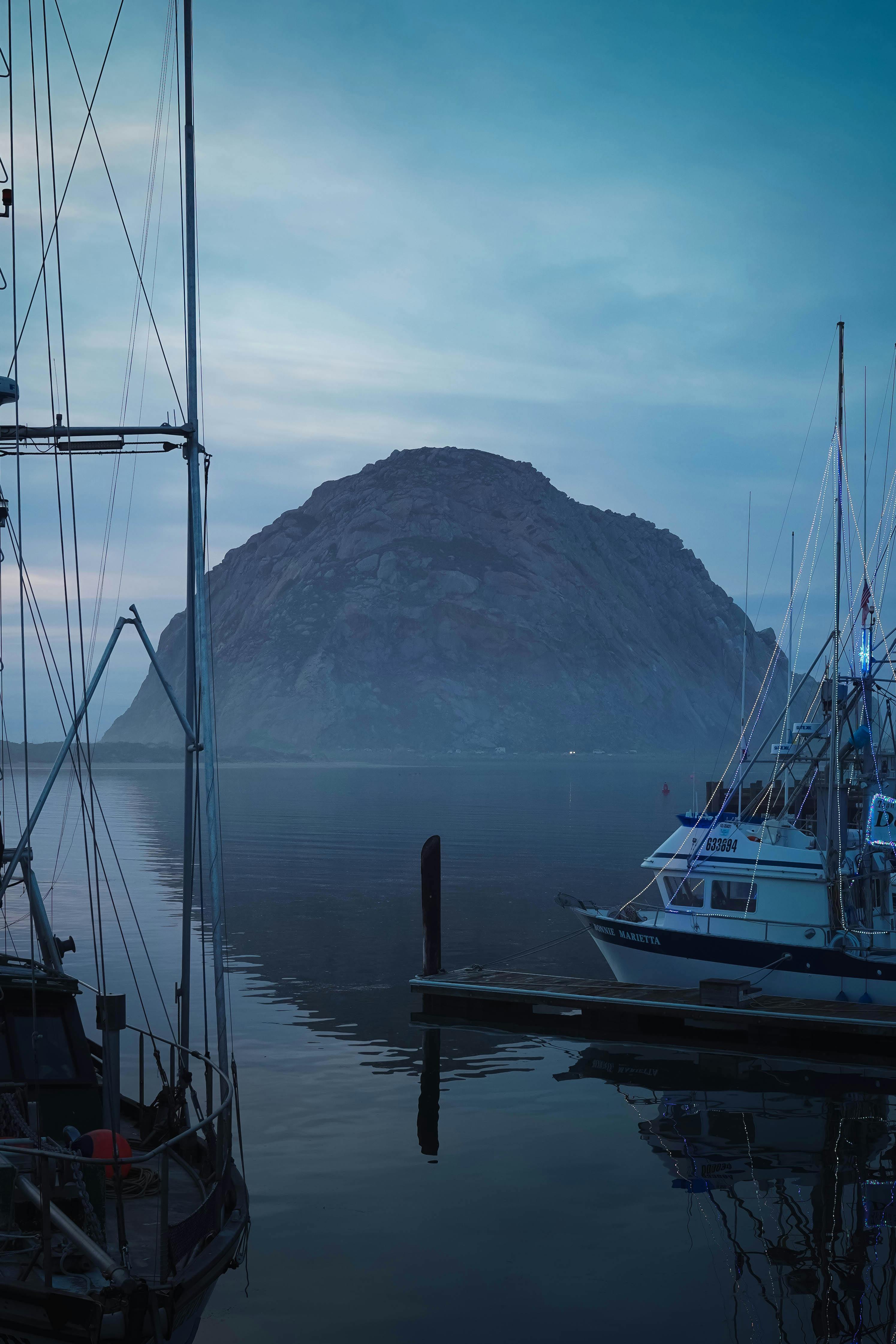 Fishing boats docked at Morro Bay during the serene blue hour, with iconic Morro Rock in the background.