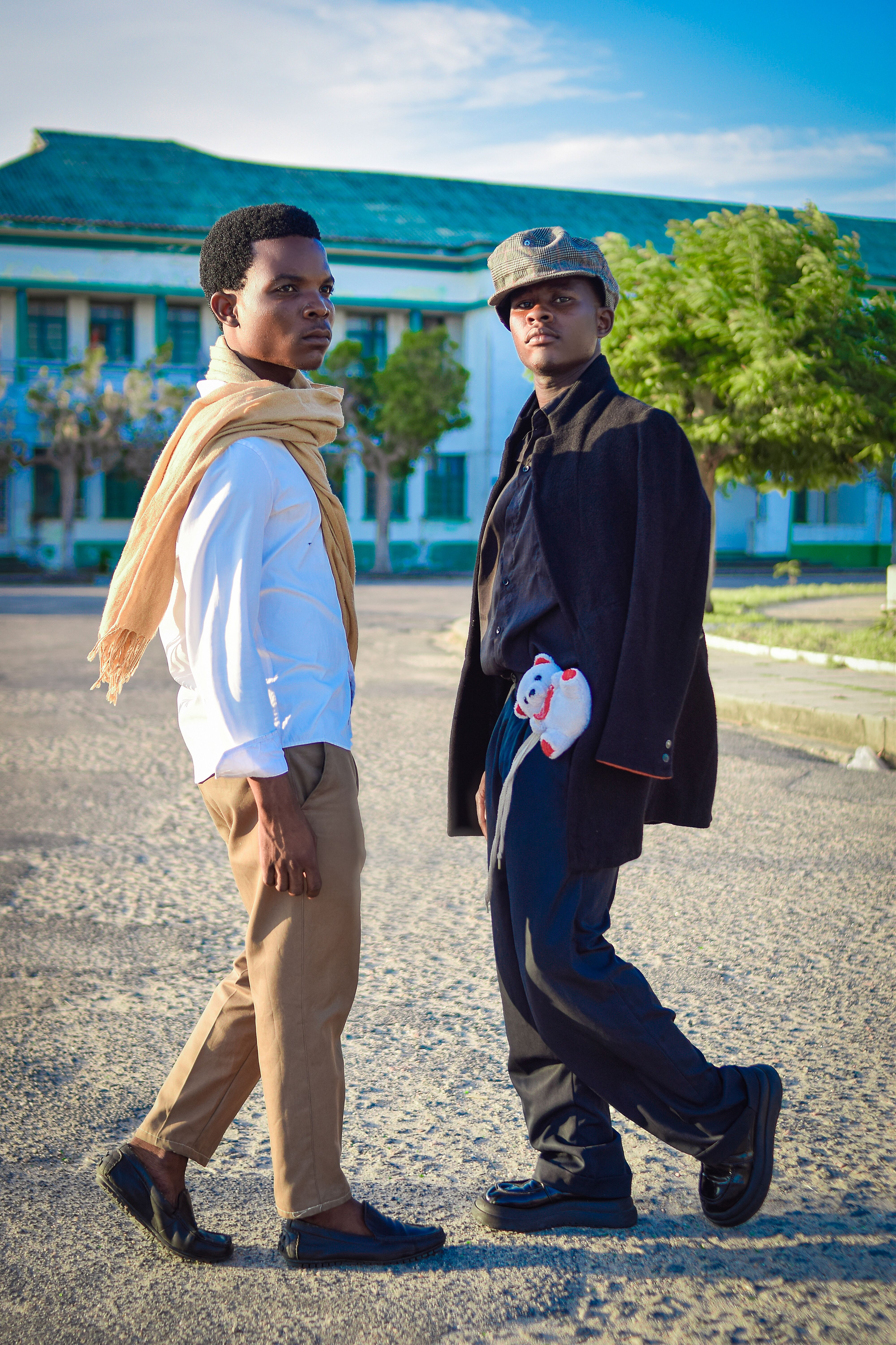 Two young men strolling in trendy outfits against a sunny backdrop, expressing modern style.