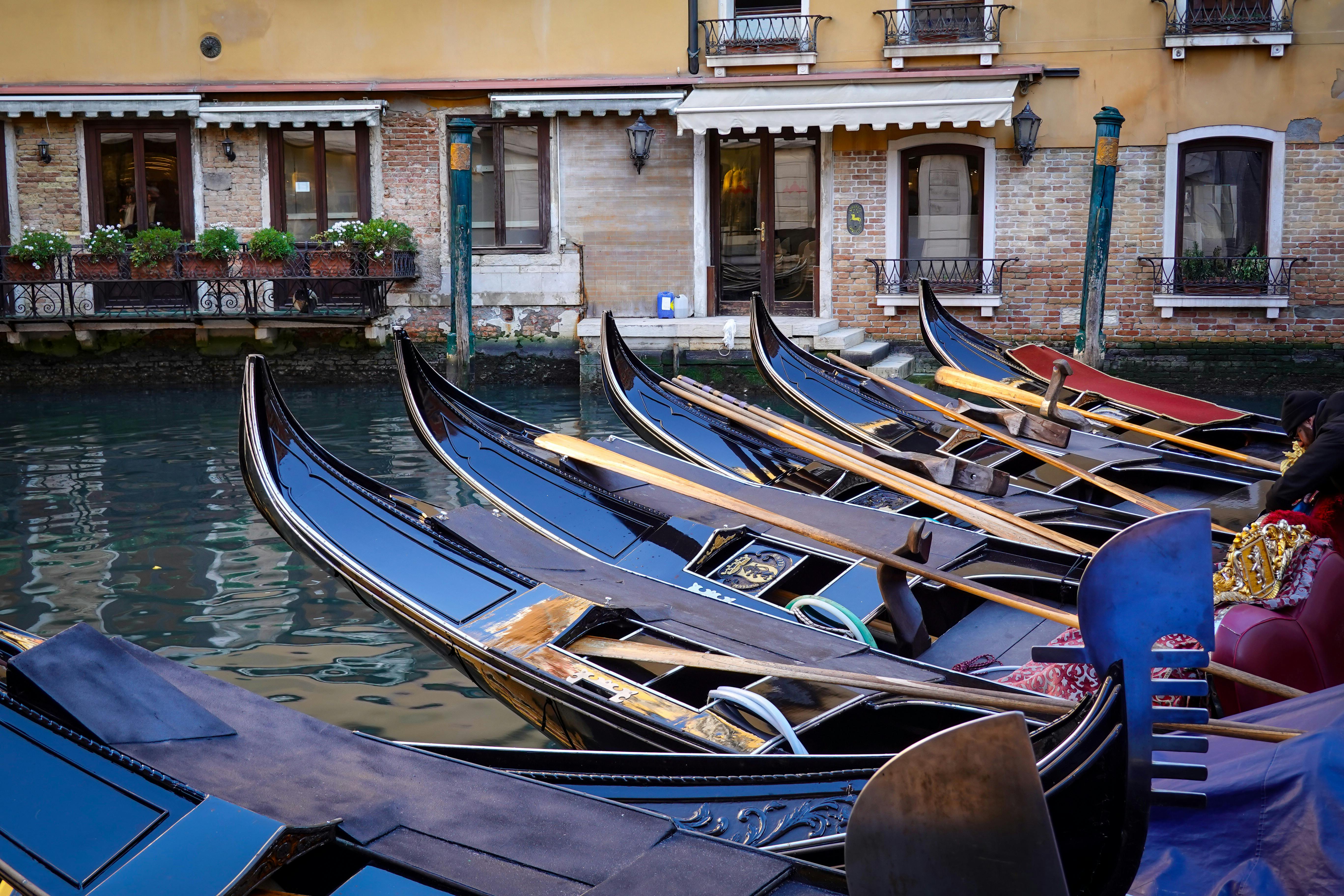 Gondolas docked by a Venetian canal, showcasing classic Italian architecture and serene water streets.