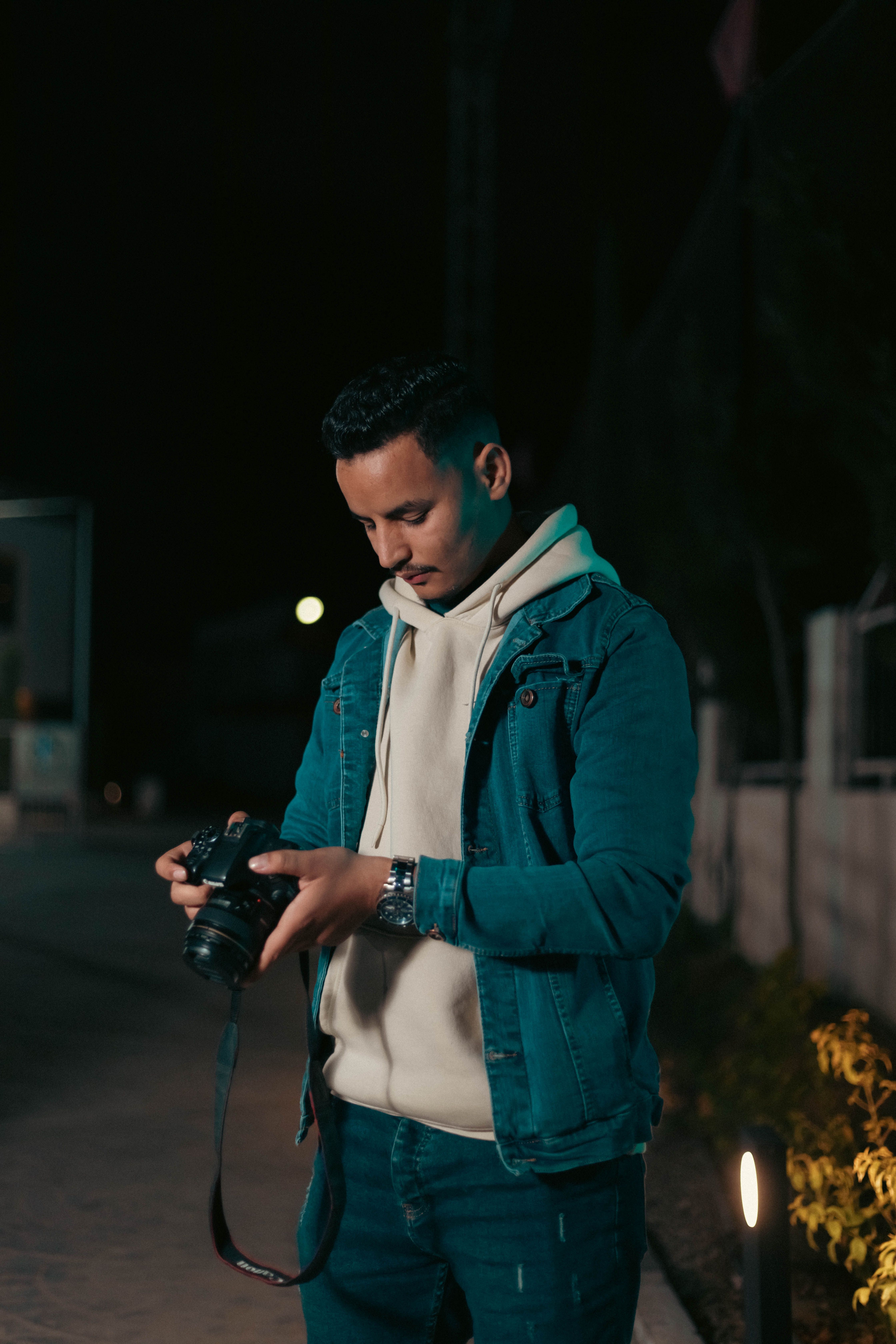 A young male photographer examines his camera in an urban night setting.