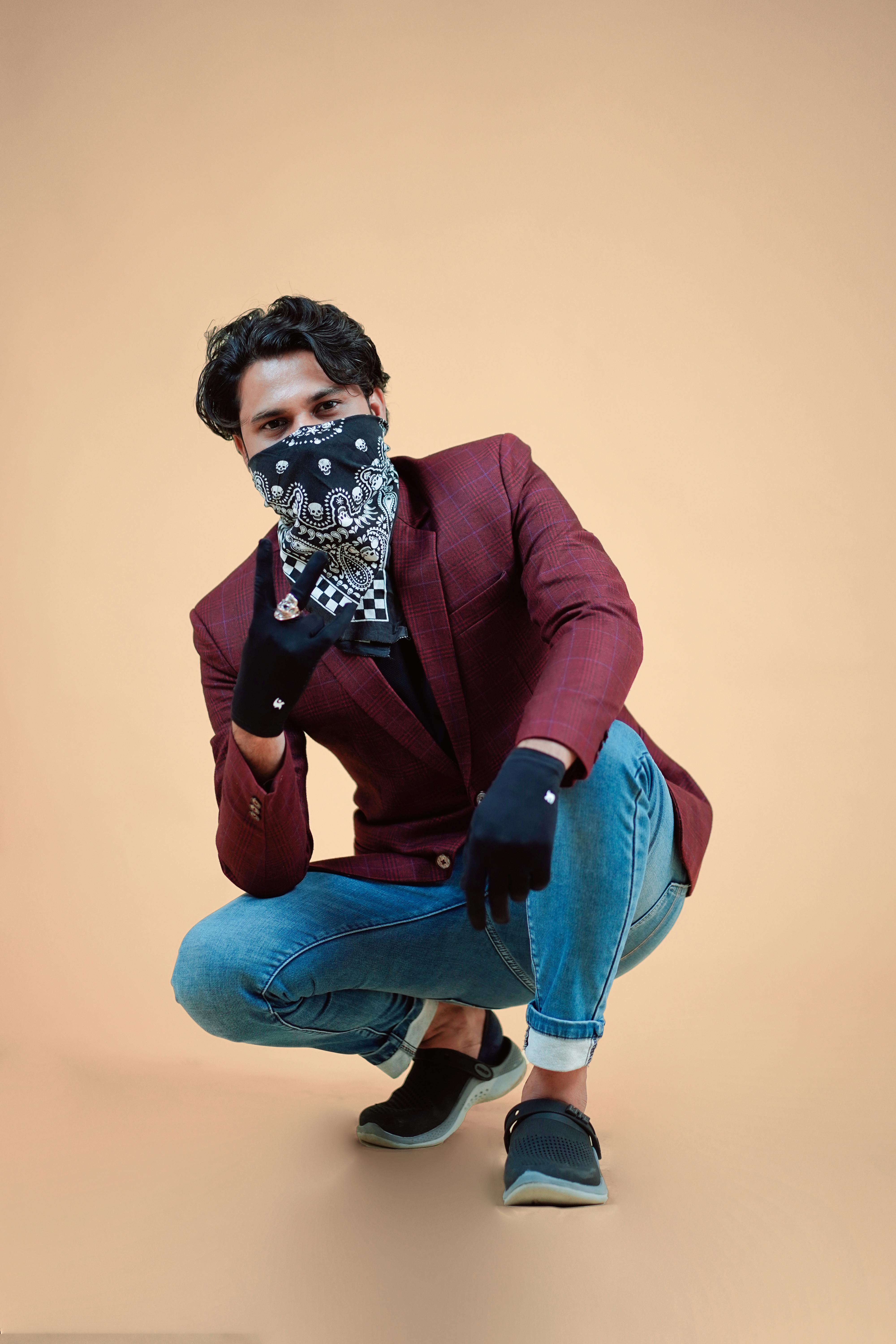 Young man in a burgundy jacket poses stylishly on a neutral background.