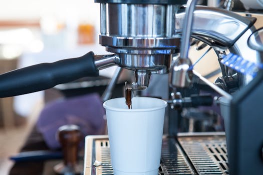 Close-up of espresso machine brewing fresh coffee into a paper cup in a café setting.