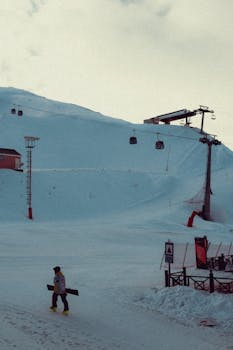 A serene winter landscape at a ski resort with a lone snowboarder.