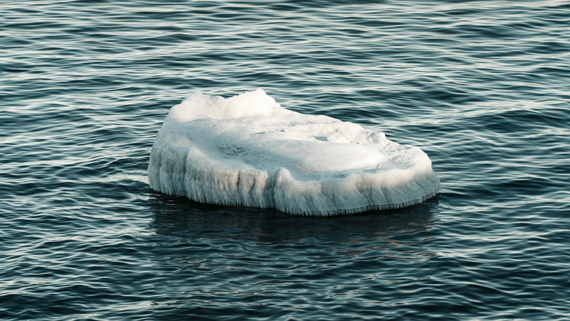 A solitary iceberg drifts through calm ocean waters, capturing a serene and tranquil scene.