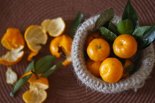 Free Vibrant mandarin oranges with leaves in a rustic basket, surrounded by peels. Stock Photo