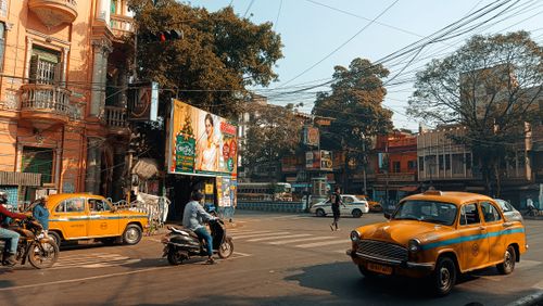 Free Vibrant street life in Kolkata featuring iconic yellow taxis and historic architecture. Stock Photo