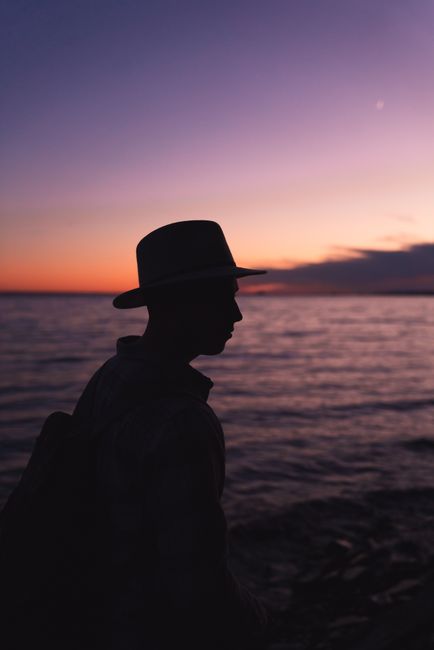 A lone man in silhouette by a serene lake during a vivid sunset in Alger County, Michigan.