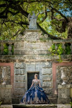 A woman in a blue gown poses gracefully in front of an ornate stone building.