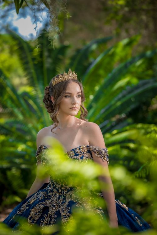 Free A graceful woman in a royal blue gown stands amidst lush garden foliage, exuding elegance. Stock Photo