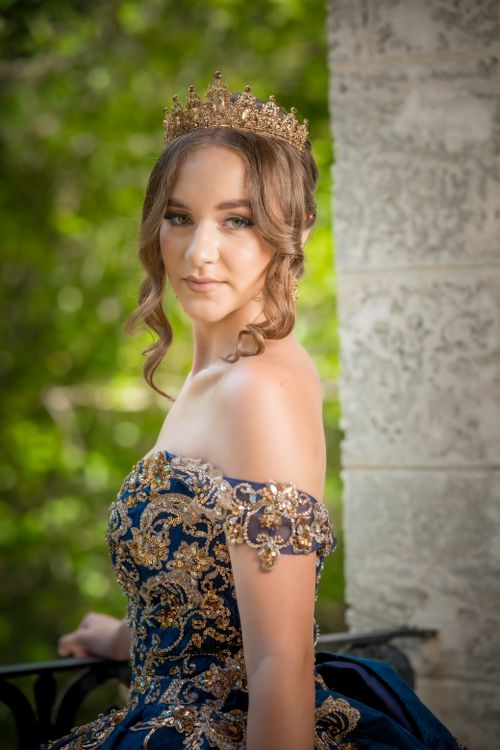 Free A woman wearing a blue and gold gown with a crown stands elegantly outdoors. Stock Photo