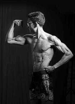 Black and white portrait of a man flexing his biceps, showcasing defined muscles.